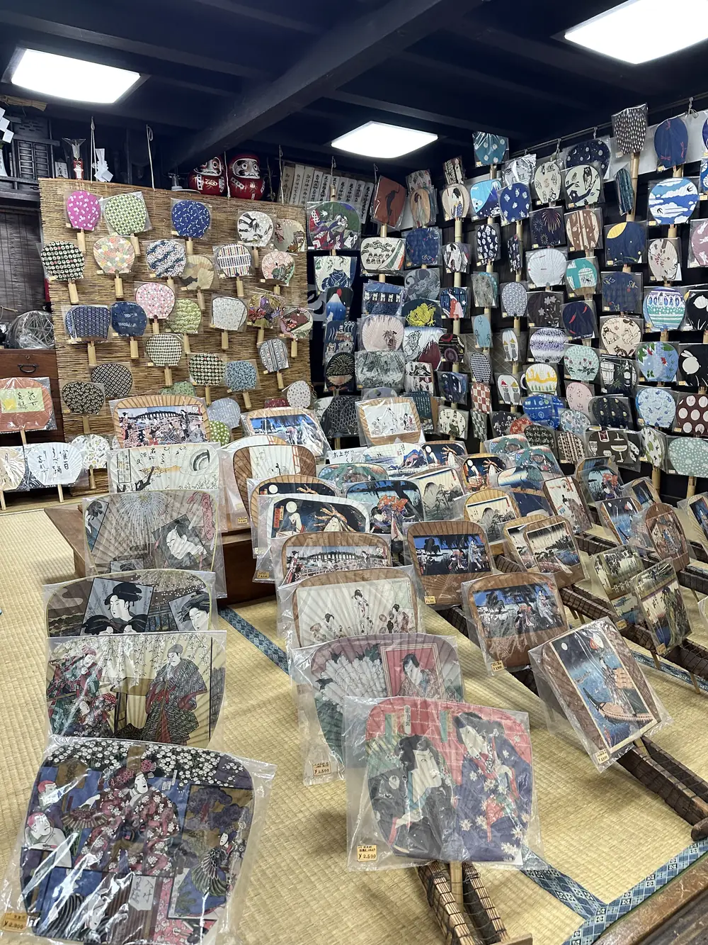 うちわ工房しまのの店内。すだれの壁と黒壁一面にうちわが並び、畳の上に浮世絵の大判うちわが立てかけられている